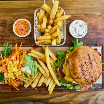 Saftiger Burger mit Salat und Pommes auf einem Holzbrett angerichtet