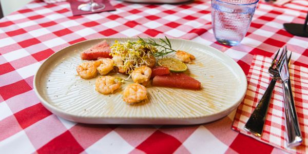 Ein länglicher Teller mit gebratenen Garnelen, Wassermelonenstücken, einer Limettenscheibe und frischen Sprossen.