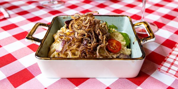 Eckige Auflaufform mit Spätzle, Röstzwiebeln und einer Kirschtomate auf rot-weiß karierter Tischdecke.